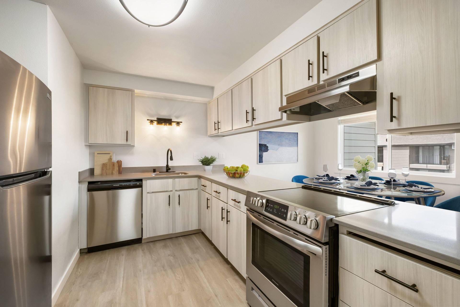 Bright modern kitchen with stainless steel appliances, white cabinets, and light wood flooring