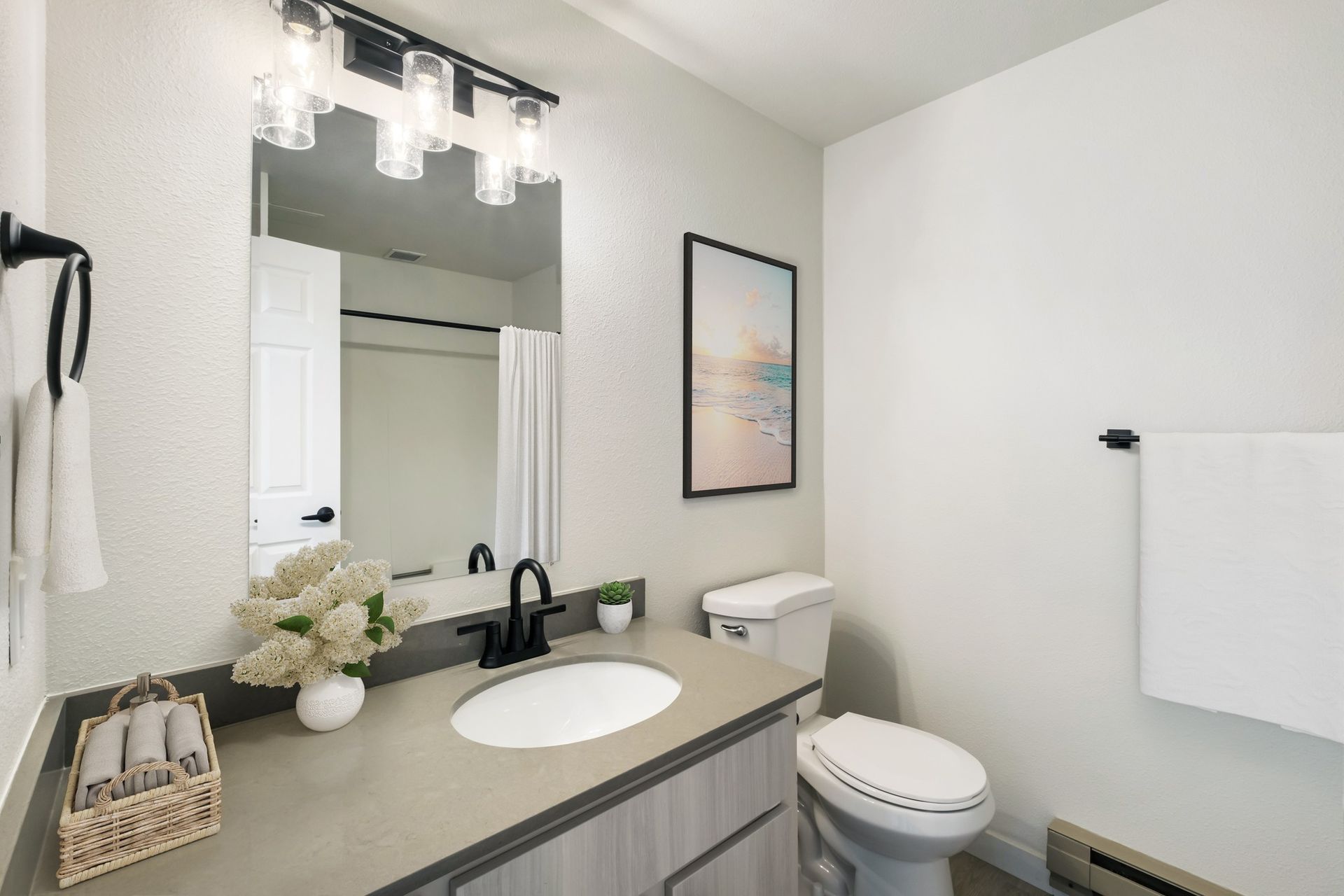 Bright modern bathroom with gray vanity, round mirror, white sink, toilet, and towel rack