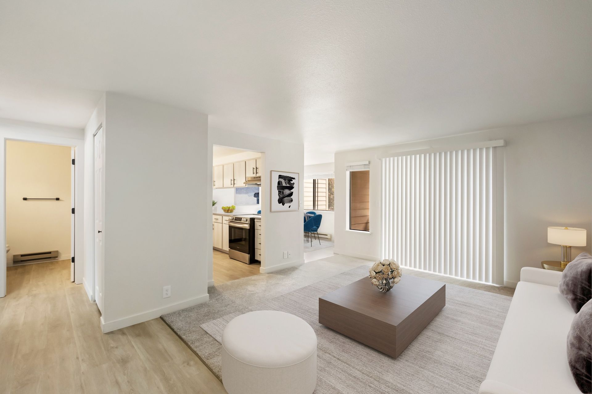 Bright modern living room with white walls, gray sofa, coffee table, and vertical blinds by the window