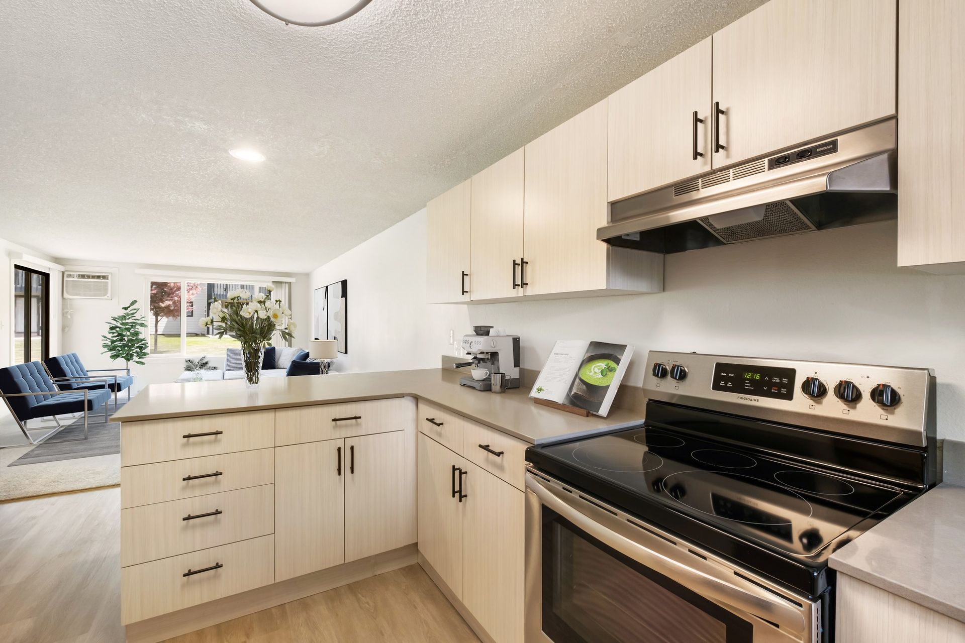 Bright modern kitchen with white cabinets, stainless steel stove, and a large island near a sunlit living area