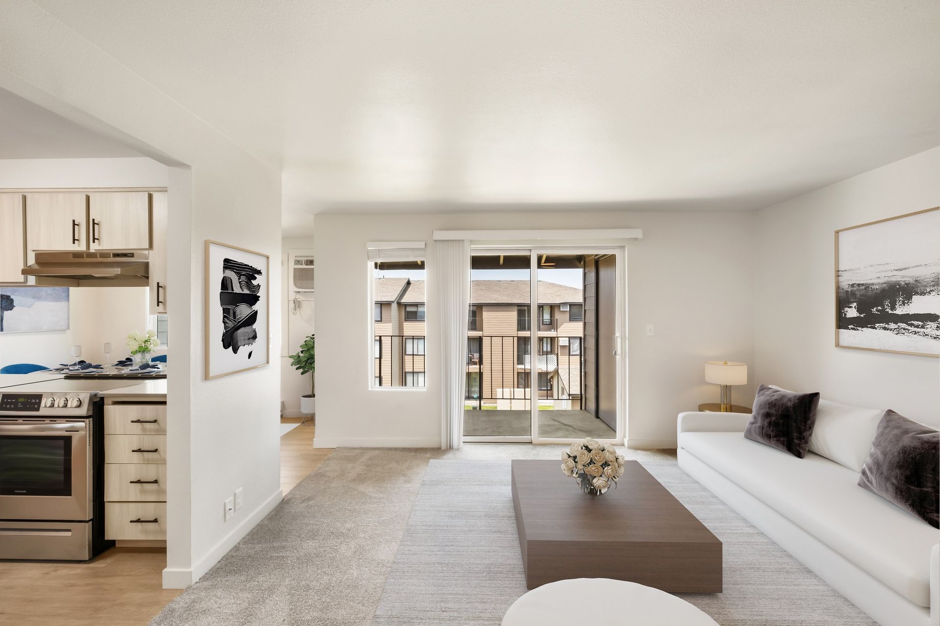 Bright modern living room with white sofa, coffee table, rug, and open kitchen view