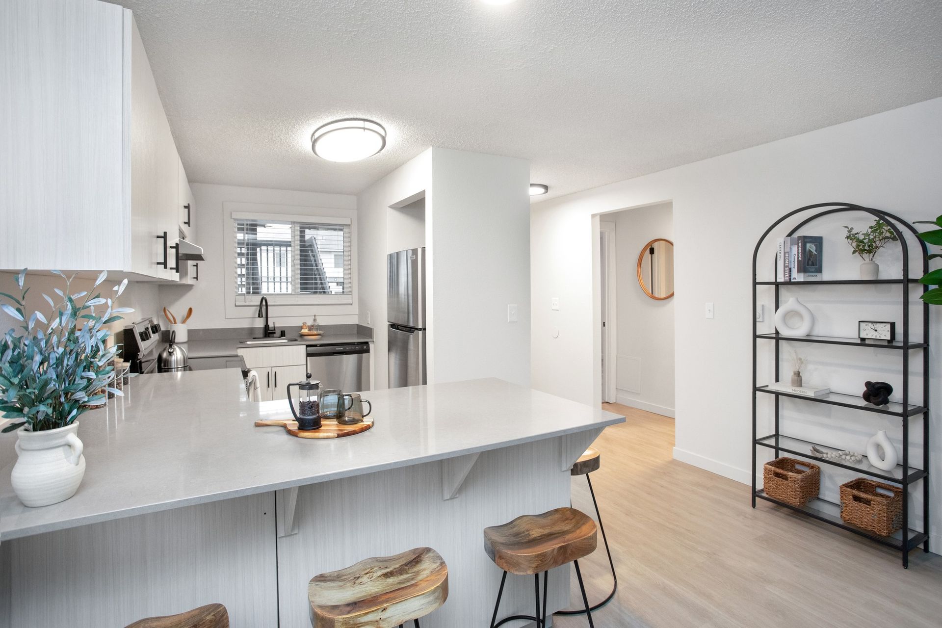 Bright modern kitchen with white cabinets, large island, stools, and open shelving in a light dining area