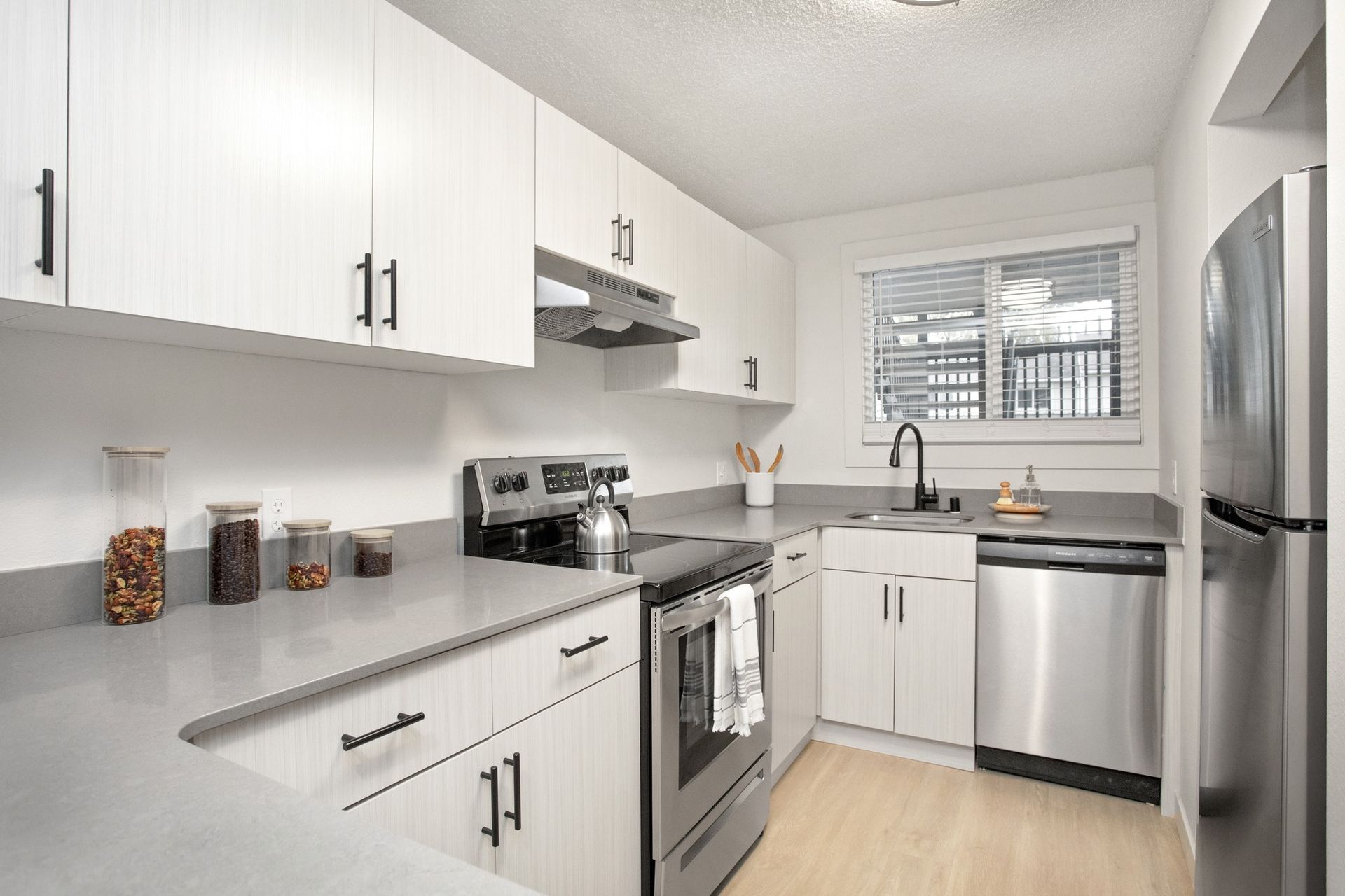 Bright modern kitchen with white cabinets, stainless steel appliances, and a window over the sink