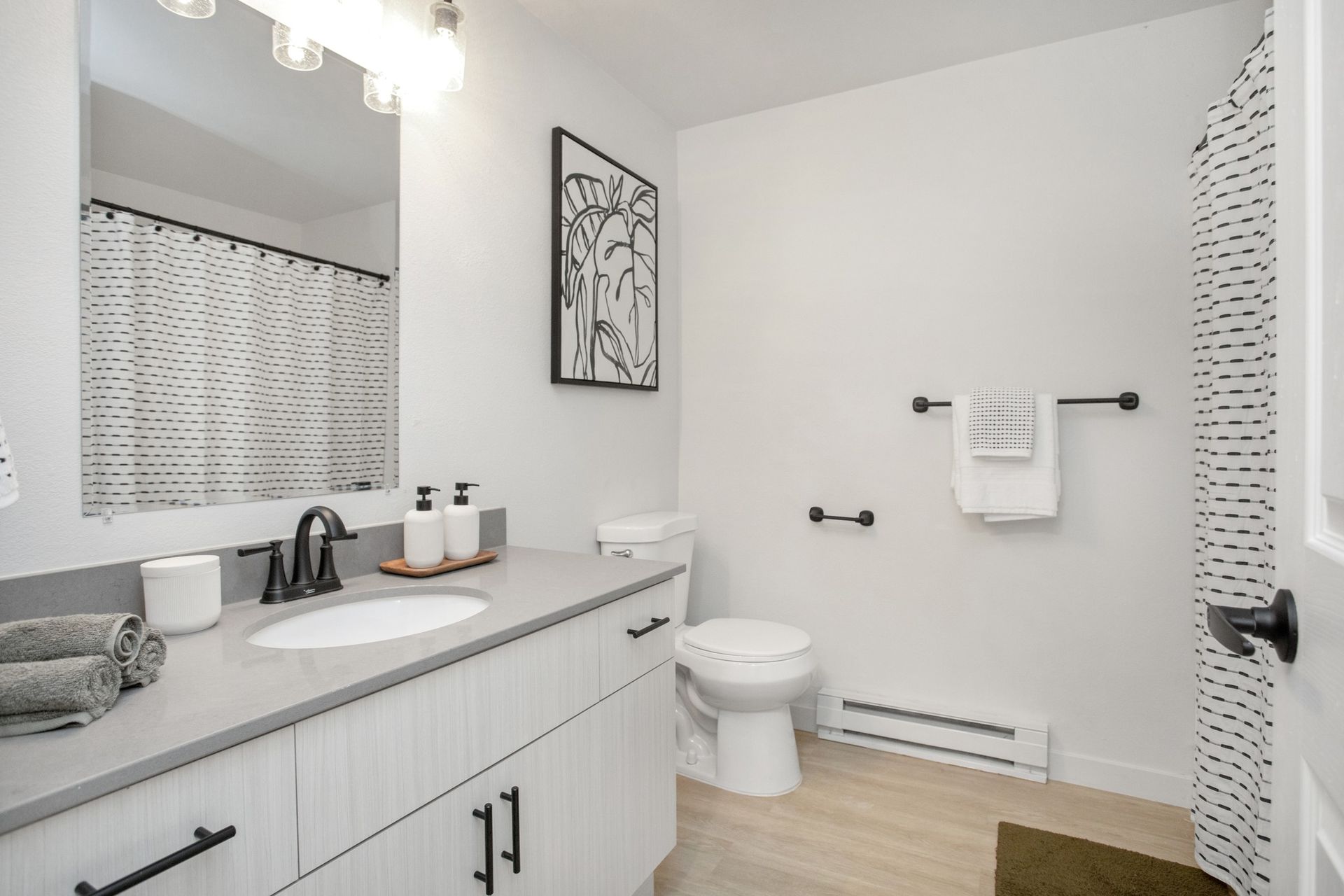 Bright bathroom with white vanity, mirror, toilet, towel bars, and patterned shower curtain