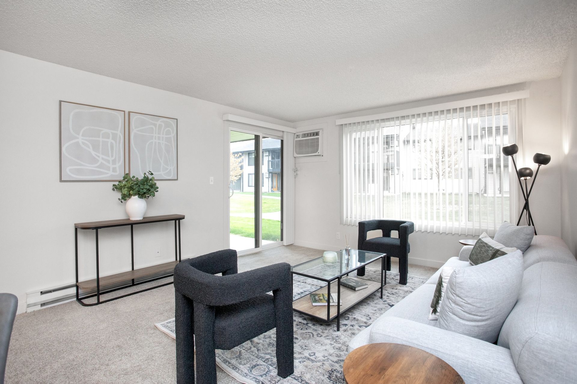 Bright living room with gray sofa, glass coffee table, black chairs, console table, and large windows.