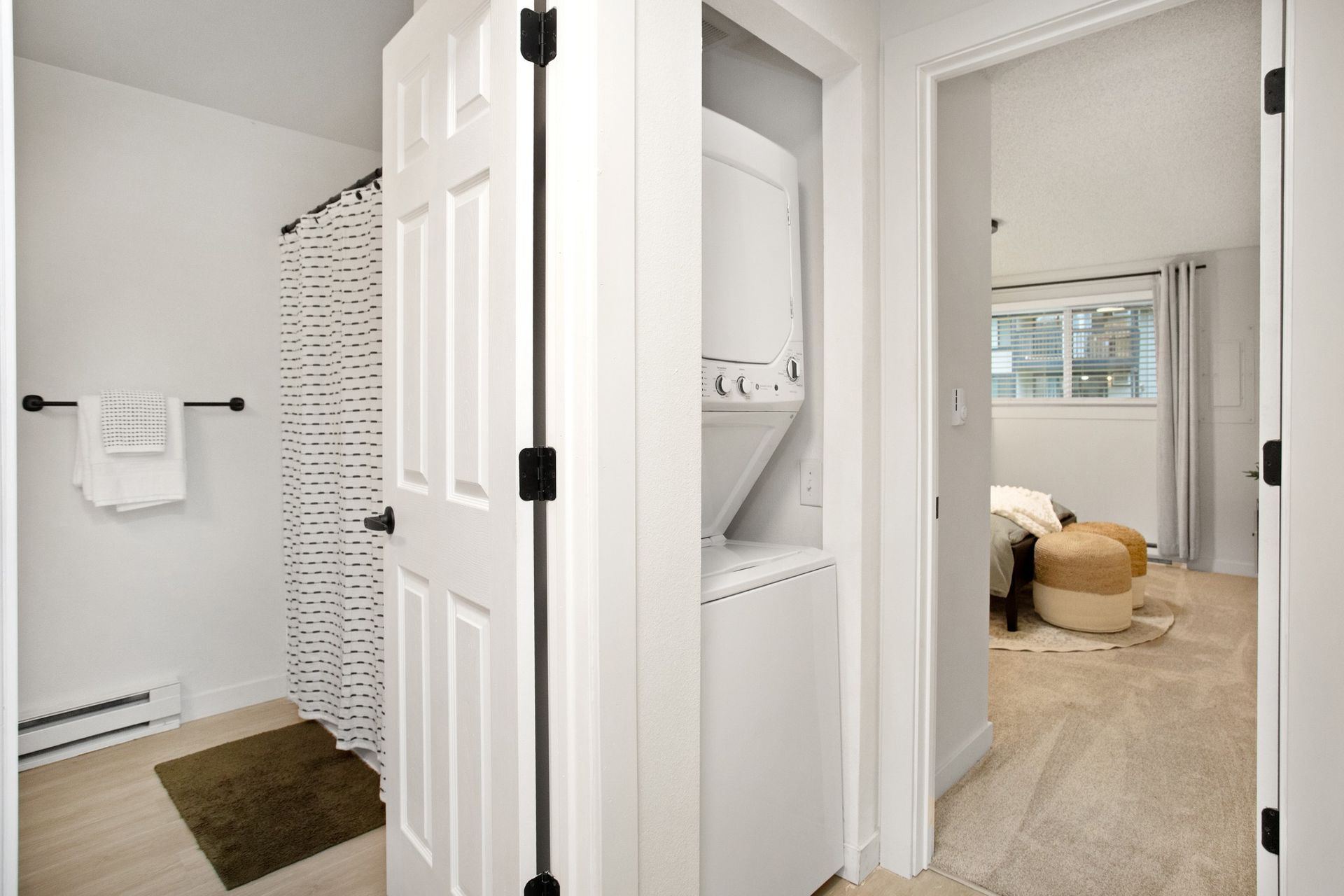 Bright bathroom hallway with white doors, tiled shower, and glimpse of a carpeted bedroom beyond.