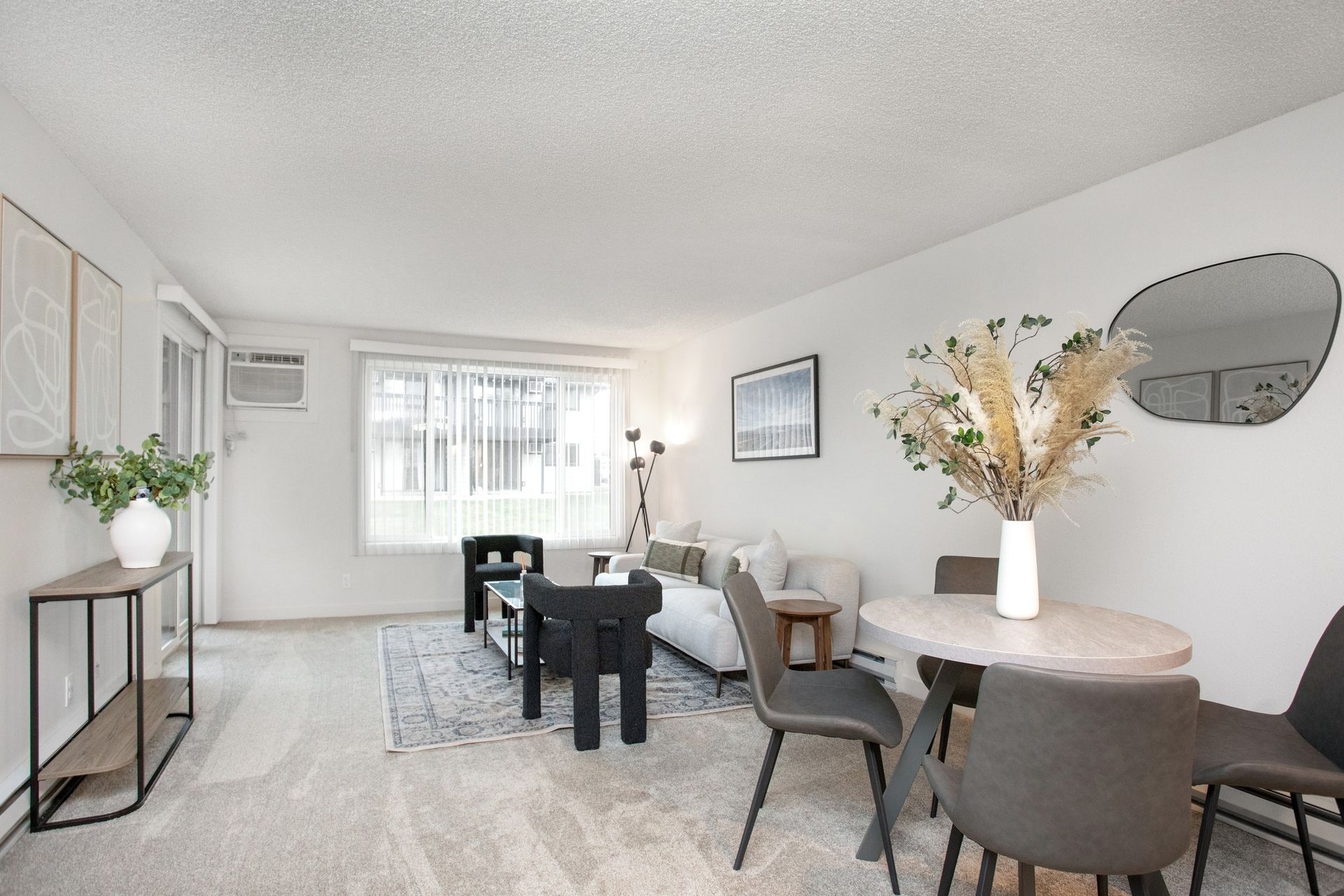 Bright living-dining room with gray sofa, round table, chairs, black console, and light decor.