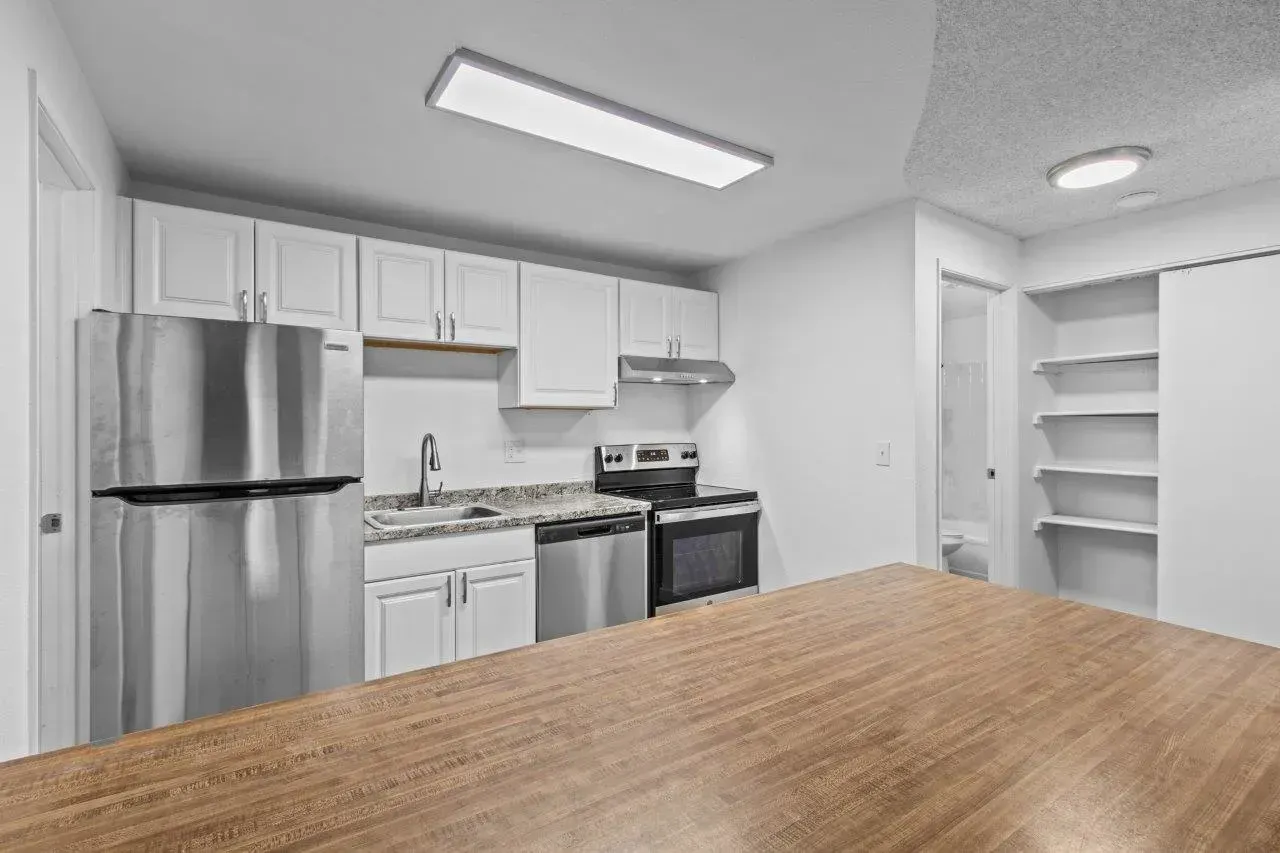 Bright kitchen with stainless steel appliances, white cabinets, and a wooden table in the foreground