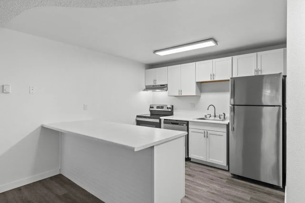 Small modern kitchen with white cabinets, stainless steel fridge, and a breakfast bar under bright lighting