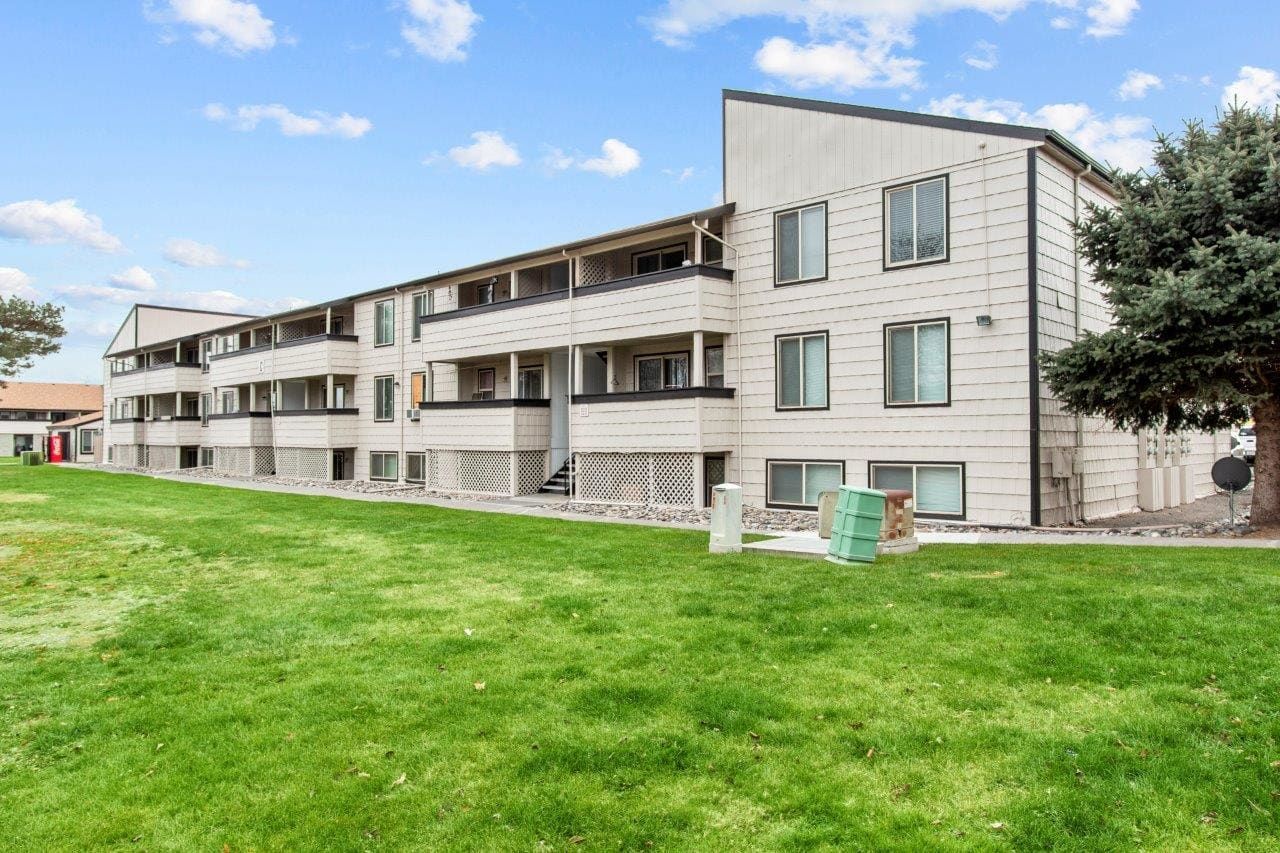 Two-story apartment building beside a green lawn under a blue sky