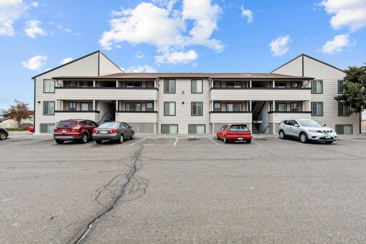 Apartment building with parked cars in front and a large gravel lot