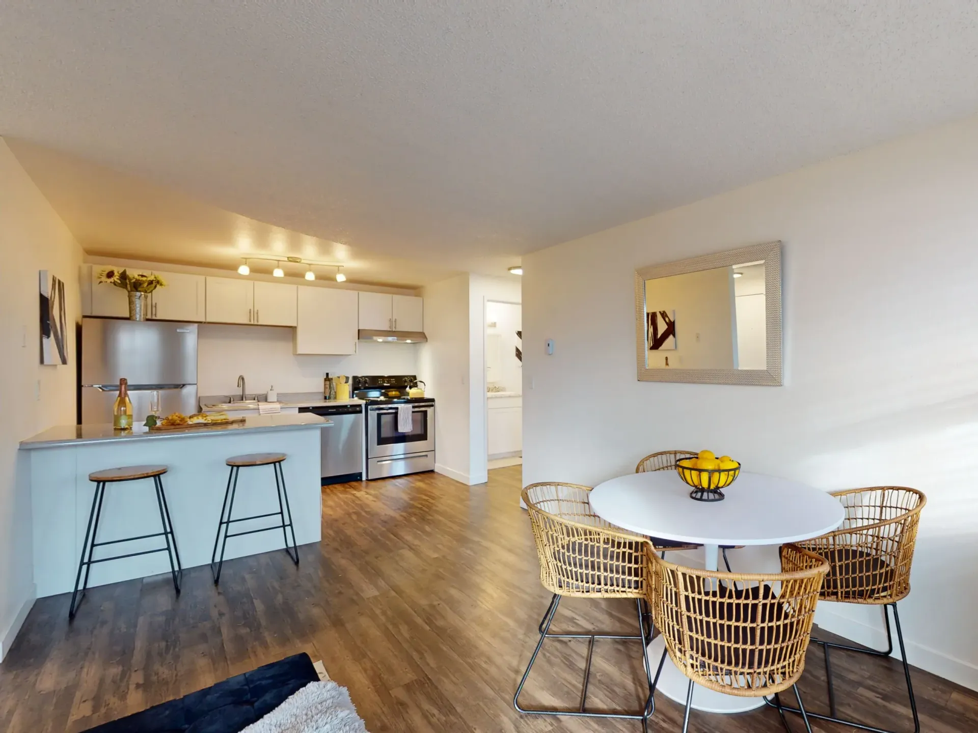 Open-plan kitchen and dining area with bar stools, round table, and wicker chairs in warm neutral tones