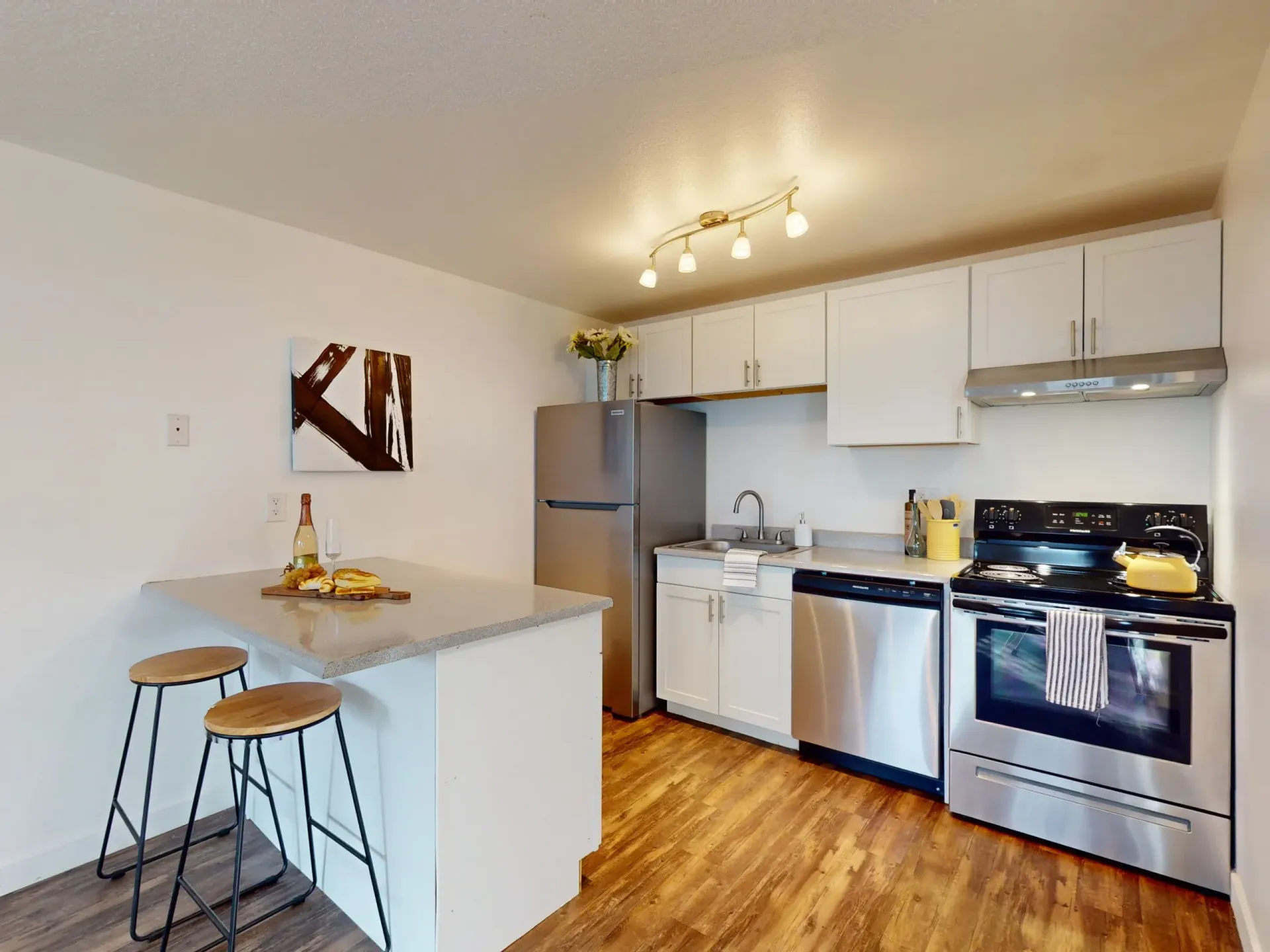 Bright modern kitchen with white cabinets, stainless steel appliances, a small island, and hardwood floors