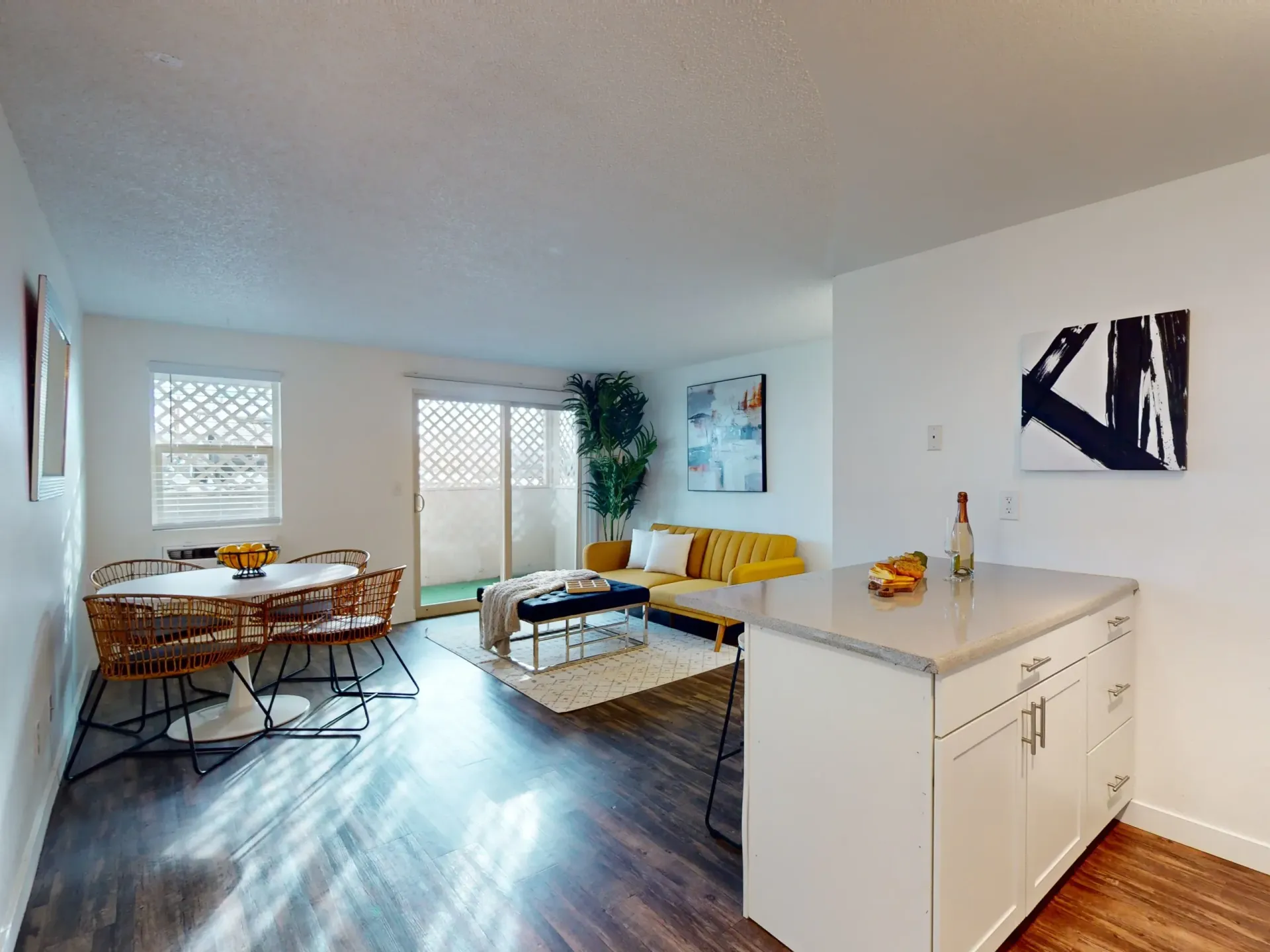 Bright open living-dining room with yellow sofa, dining table, white kitchen island, and large windows