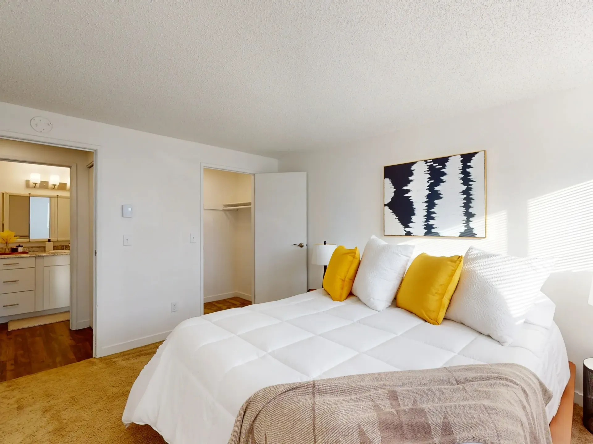 Bright bedroom with a white bed, yellow pillows, open closet, and bathroom doorway.