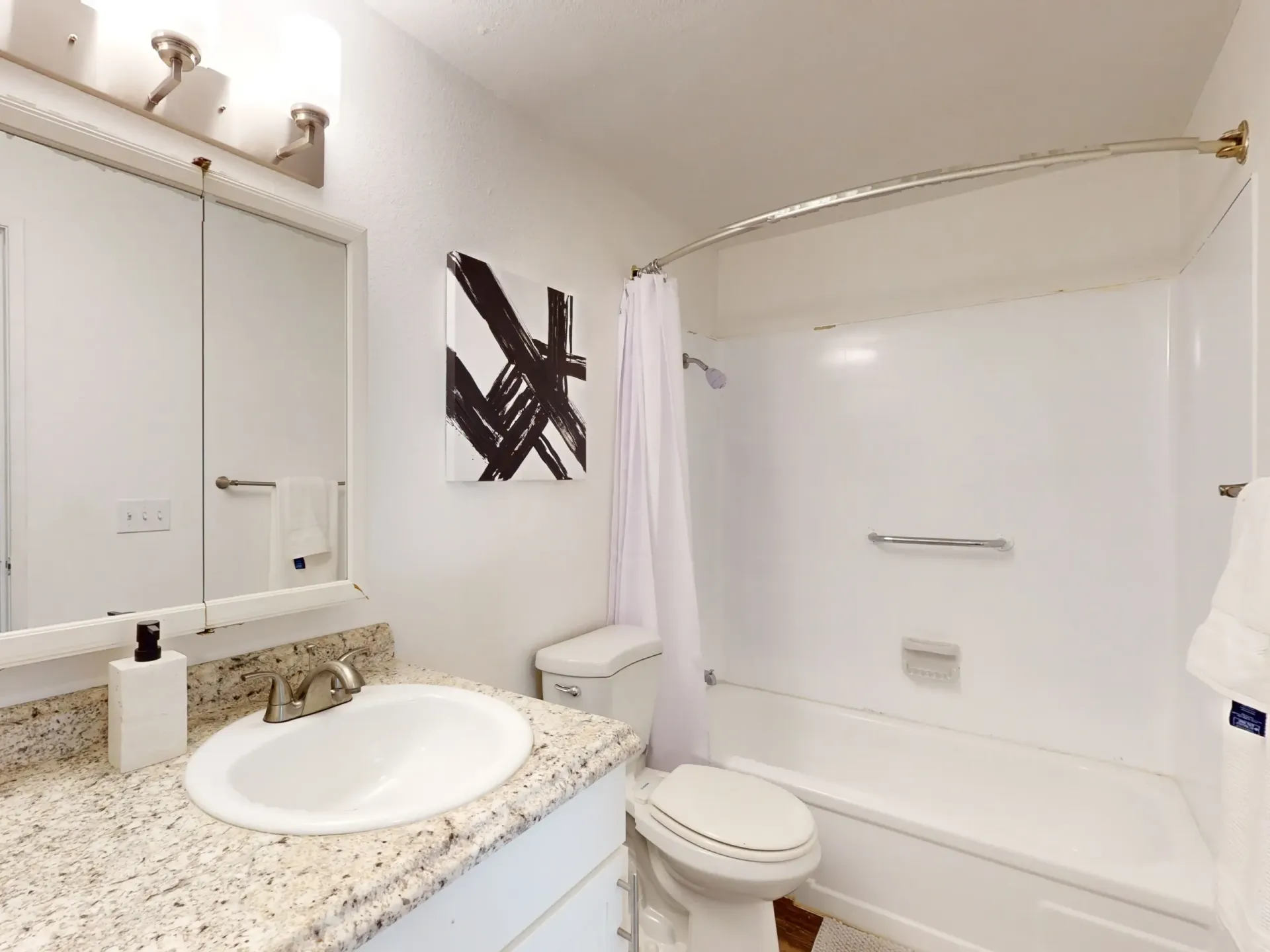 Bright bathroom with white tub-shower, toilet, sink, mirrored cabinet, and beige granite countertop.