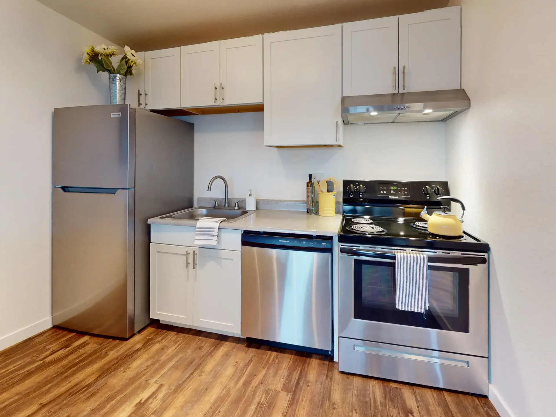 Small kitchen with stainless steel refrigerator, white cabinets, and black stove on a wood floor.