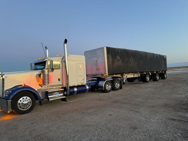 White and blue semi-truck with a trailer on a gray surface against a light blue sky.