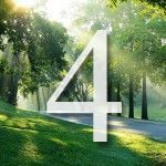 The number four is surrounded by trees and grass in a park.