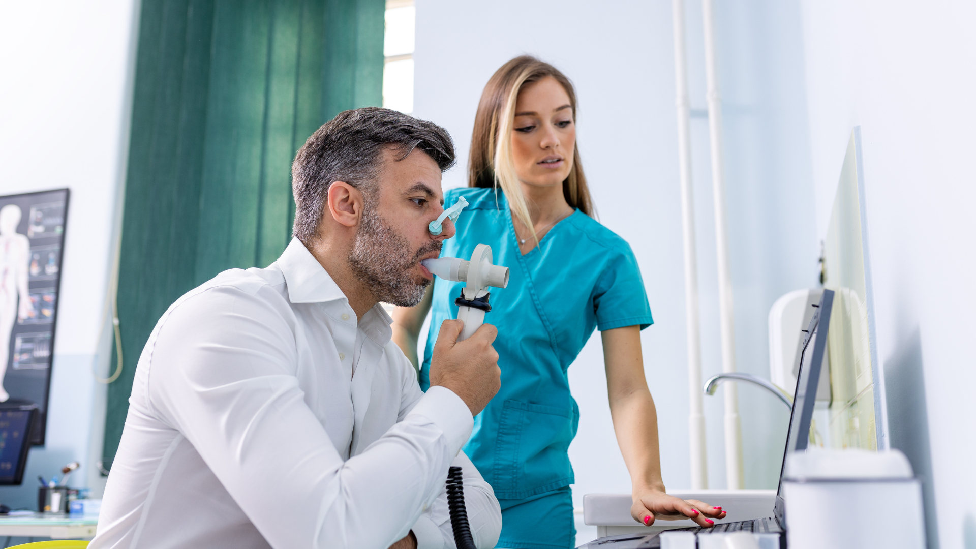Man taking a breathing test with a nurse in a medical setting, both looking at the screen.