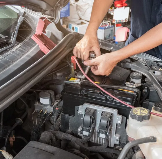 Mechanic using jumper cables in a car engine bay, with the hood open.