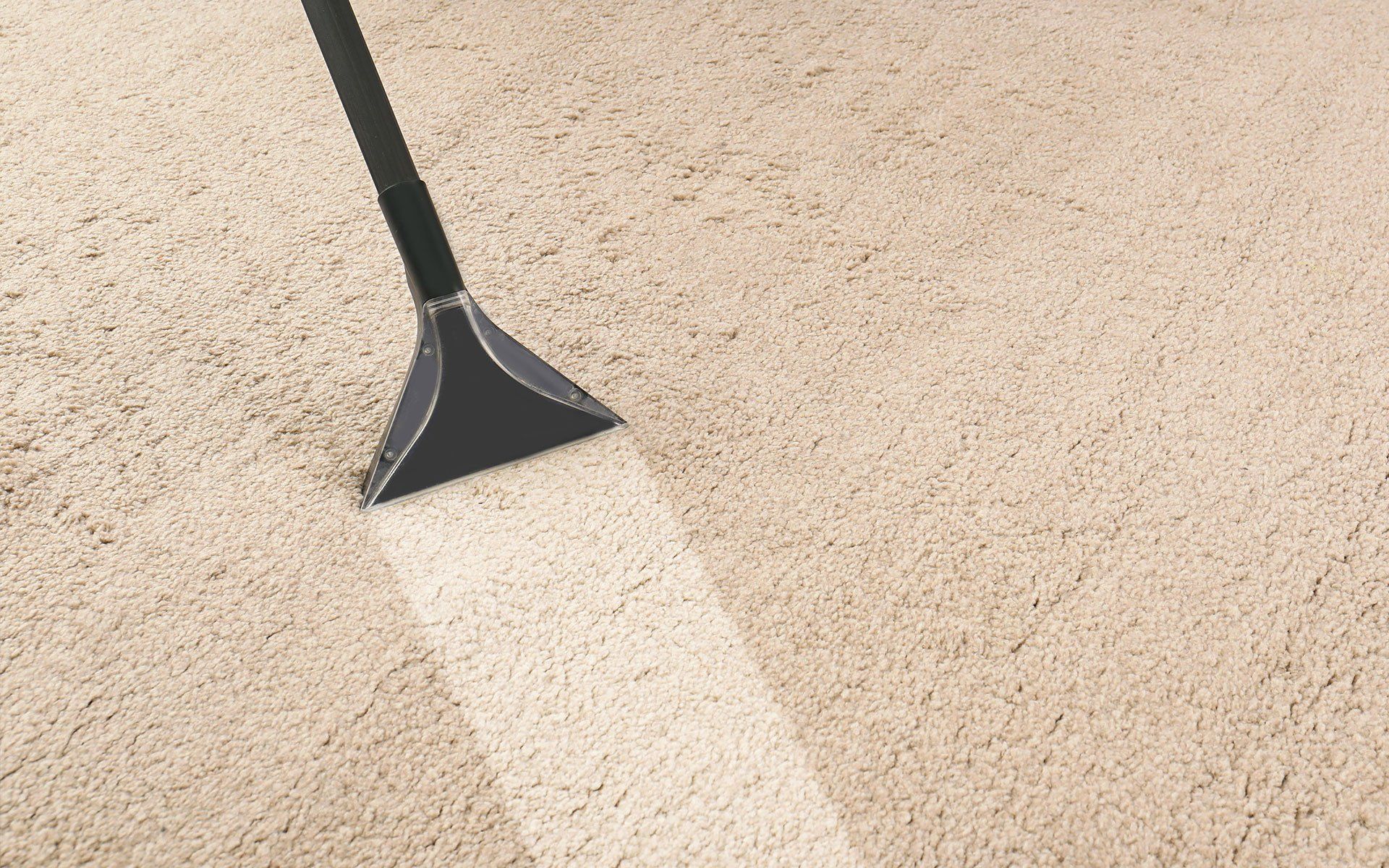 Carpet cleaner nozzle spraying a white stream on beige carpet