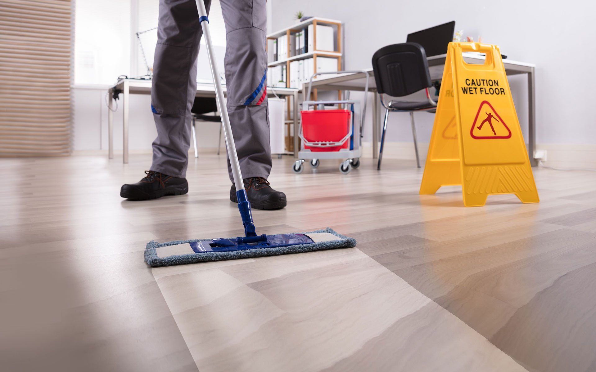 Person mopping a hardwood floor with a yellow wet floor sign in a hallway
