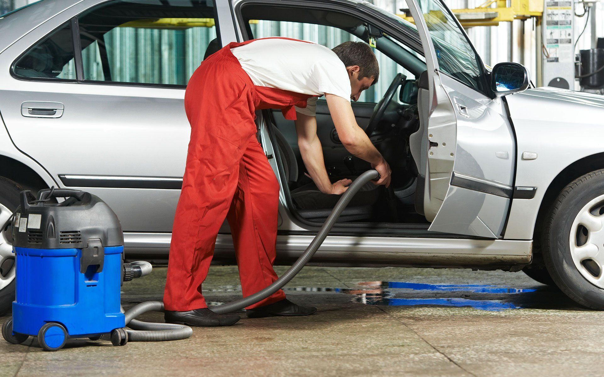 Car detailer vacuuming the interior of a silver car with the driver door open