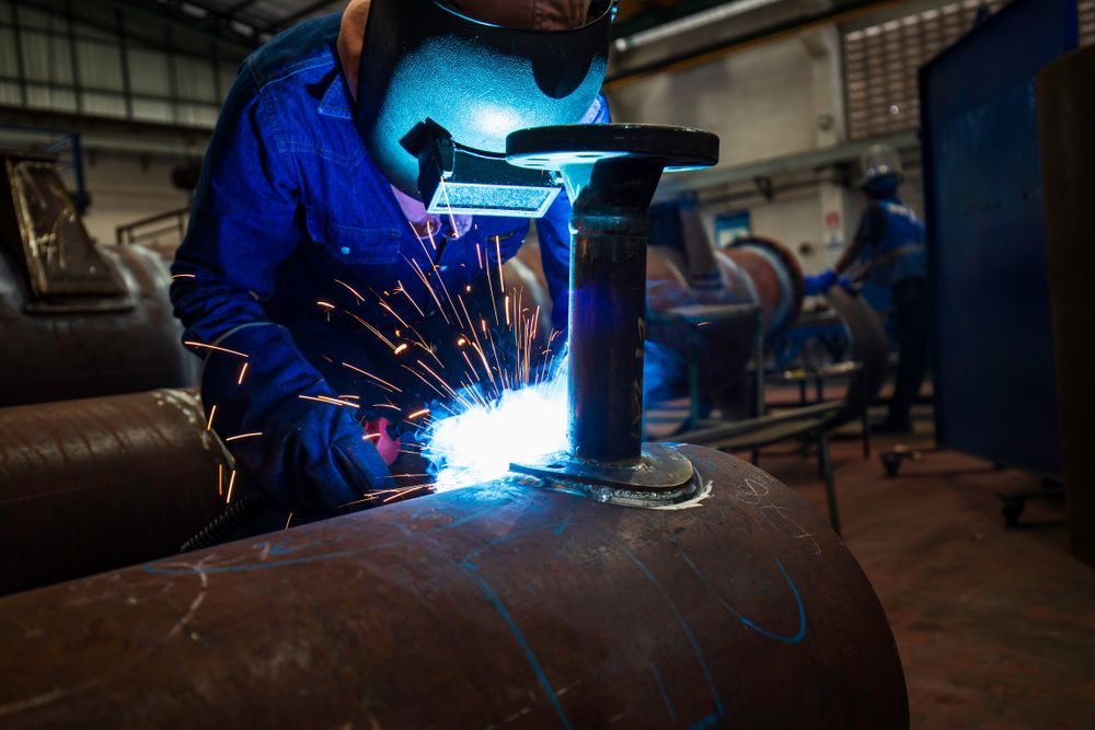 A Man Is Welding A Pipe In A Factory — Tinman's Welding Worx In Sarina, QLD