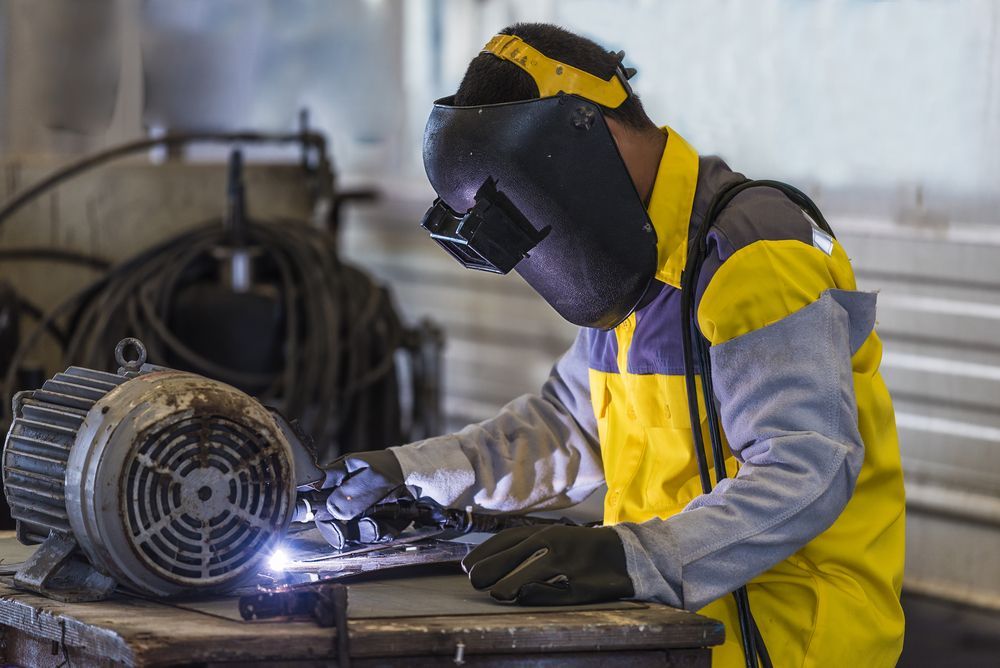 A man wearing a welding mask is welding a motor — Tinman's Welding Worx In Sarina, QLD