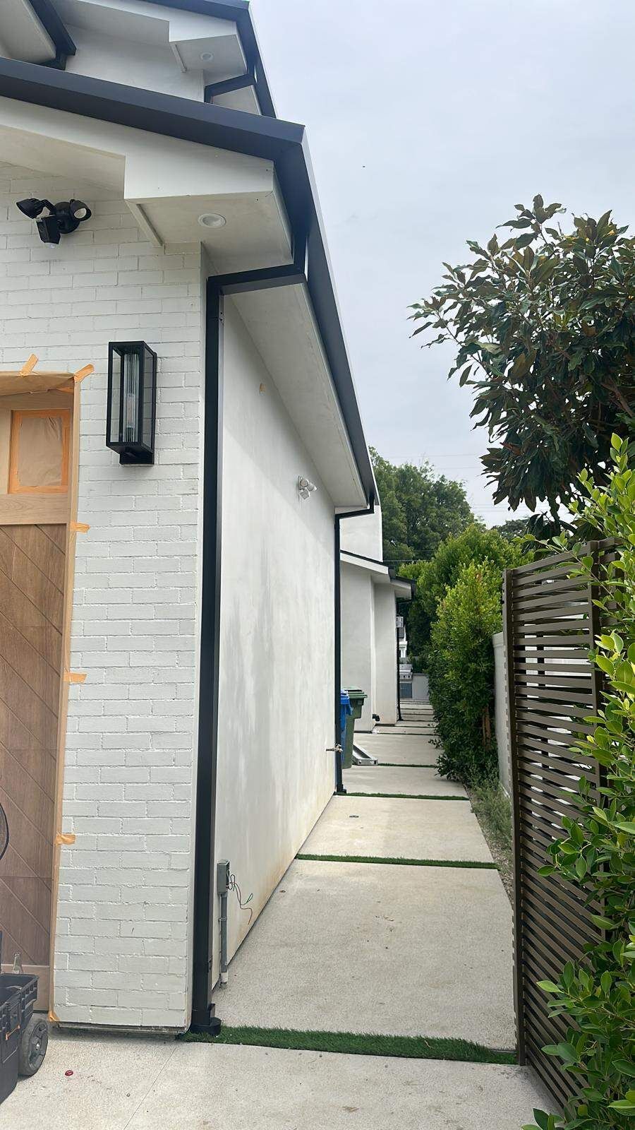 A side view of a white brick house with black trim and a modern, paved pathway leading toward the backyard.