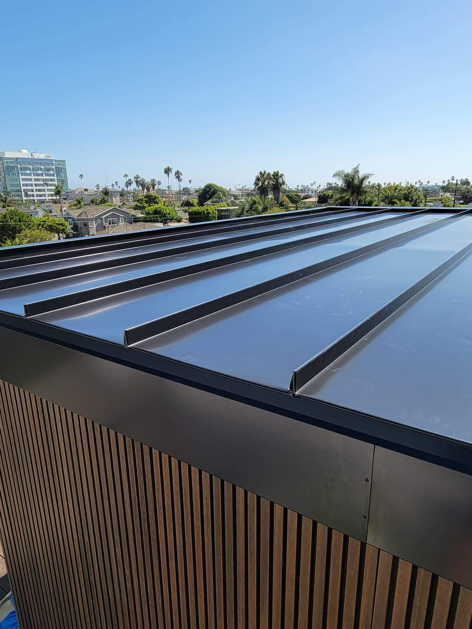 A low-angle view of a flat roof with dark metal standing seams, featuring wood-slat siding on a sunny day.
