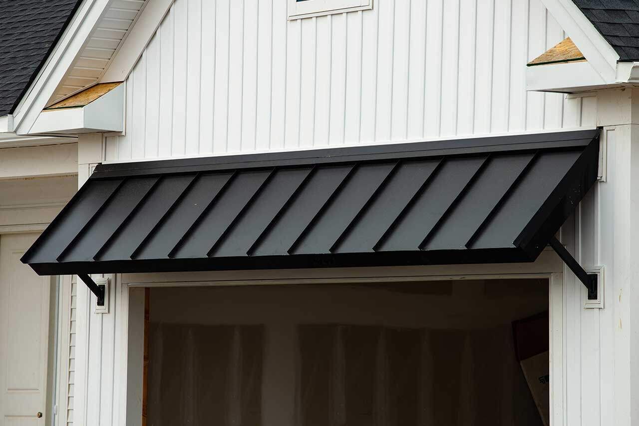 A black metal shed roof awning installed over a garage door opening on a white building.