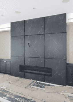 A large, dark gray, marbled stone fireplace wall with a horizontal firebox, shown during home construction.