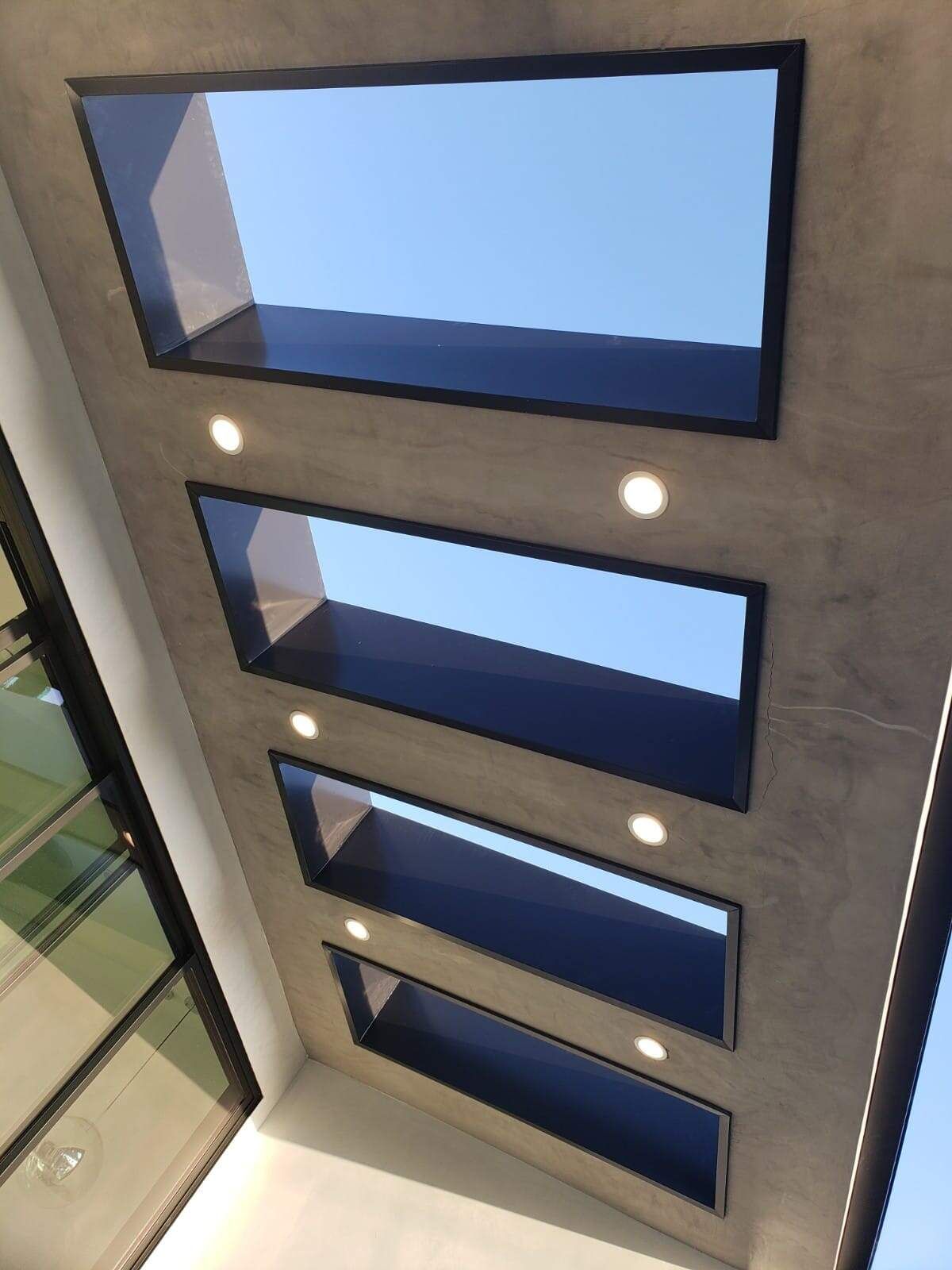 A series of four rectangular skylights set into a textured, dark gray ceiling with integrated circular recessed lights.