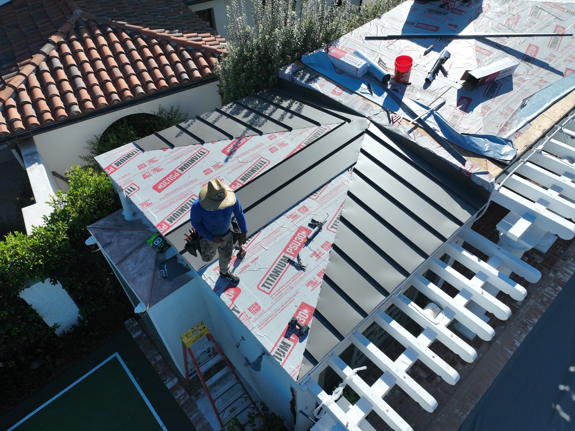 Workers installing roofing on a house with red tiles and white roof panels