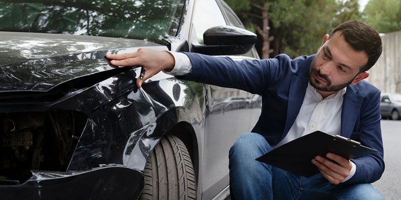 A man is kneeling down in front of a damaged car.