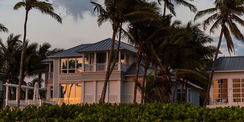 A large white house with a blue roof is surrounded by palm trees.
