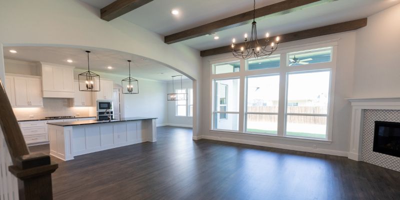 An empty living room in a house with a fireplace and a kitchen.