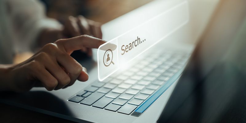 A person is using a laptop computer with a search bar on the screen.