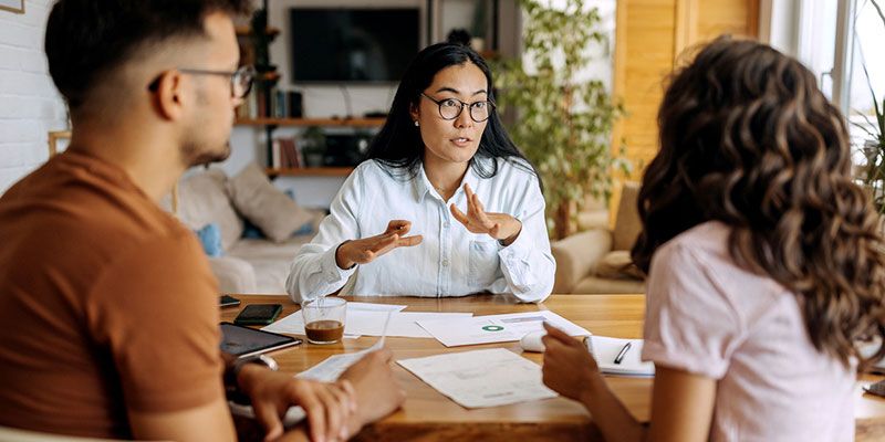 A woman is sitting at a table talking to a man and a woman.