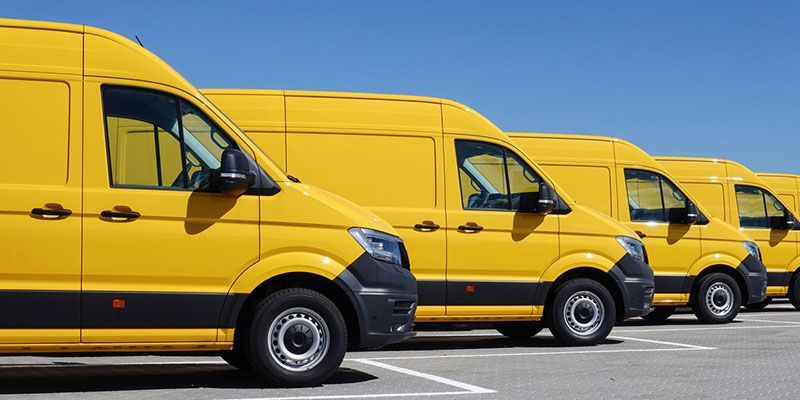 A row of yellow delivery vans are parked in a parking lot.