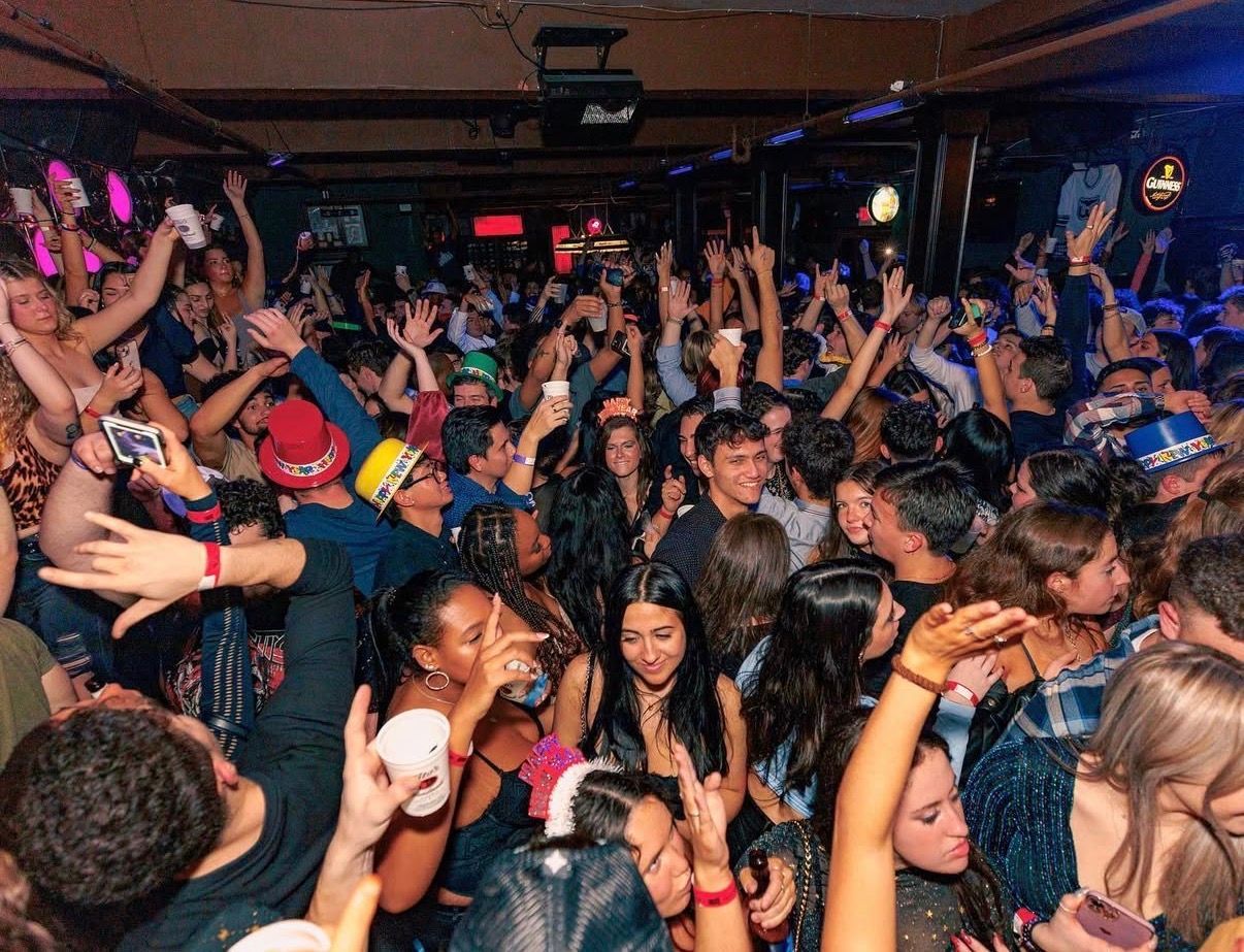 Crowded nightclub dance floor with people raising their hands under colorful lights