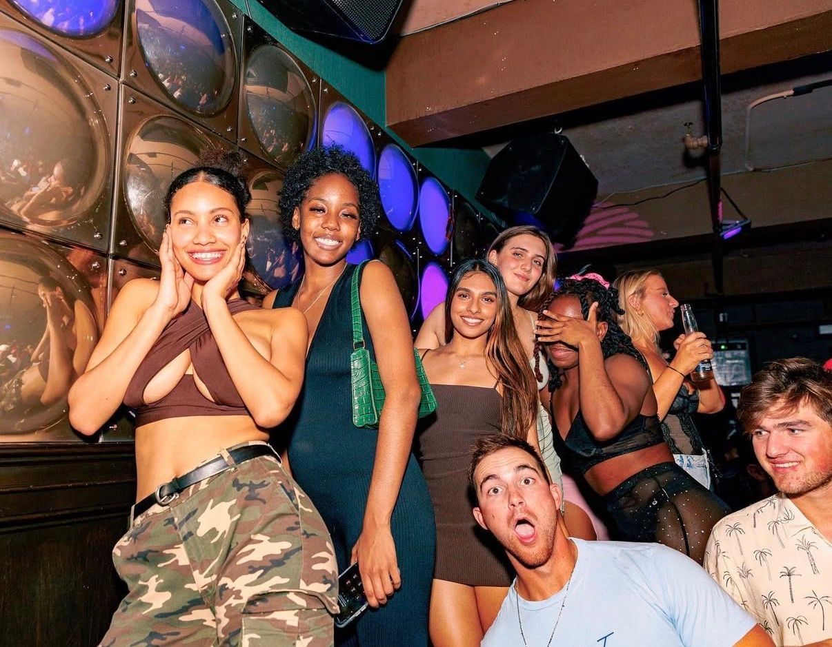 Group of friends posing and dancing in a lively nightclub with colorful lights and mirrored walls at the Lady Hartford