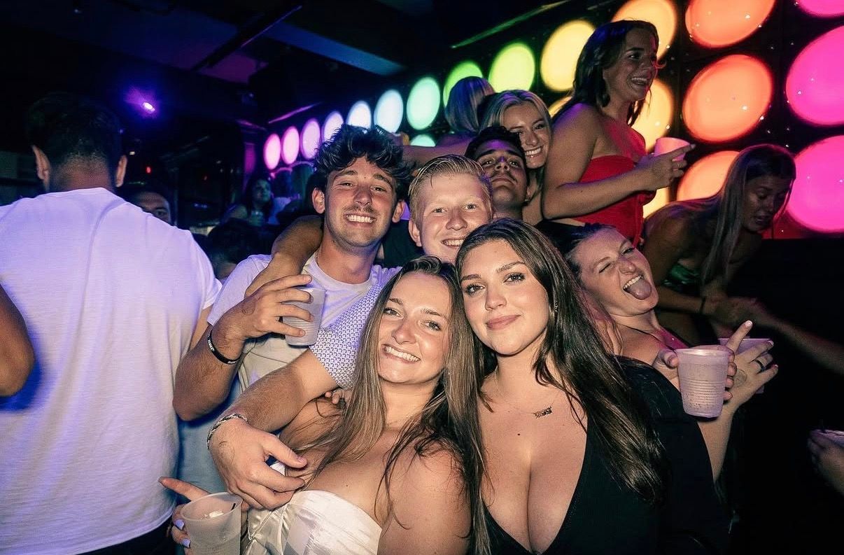 Crowded party scene with smiling people in colorful neon lighting, posing and holding drinks at the Lady Hartford