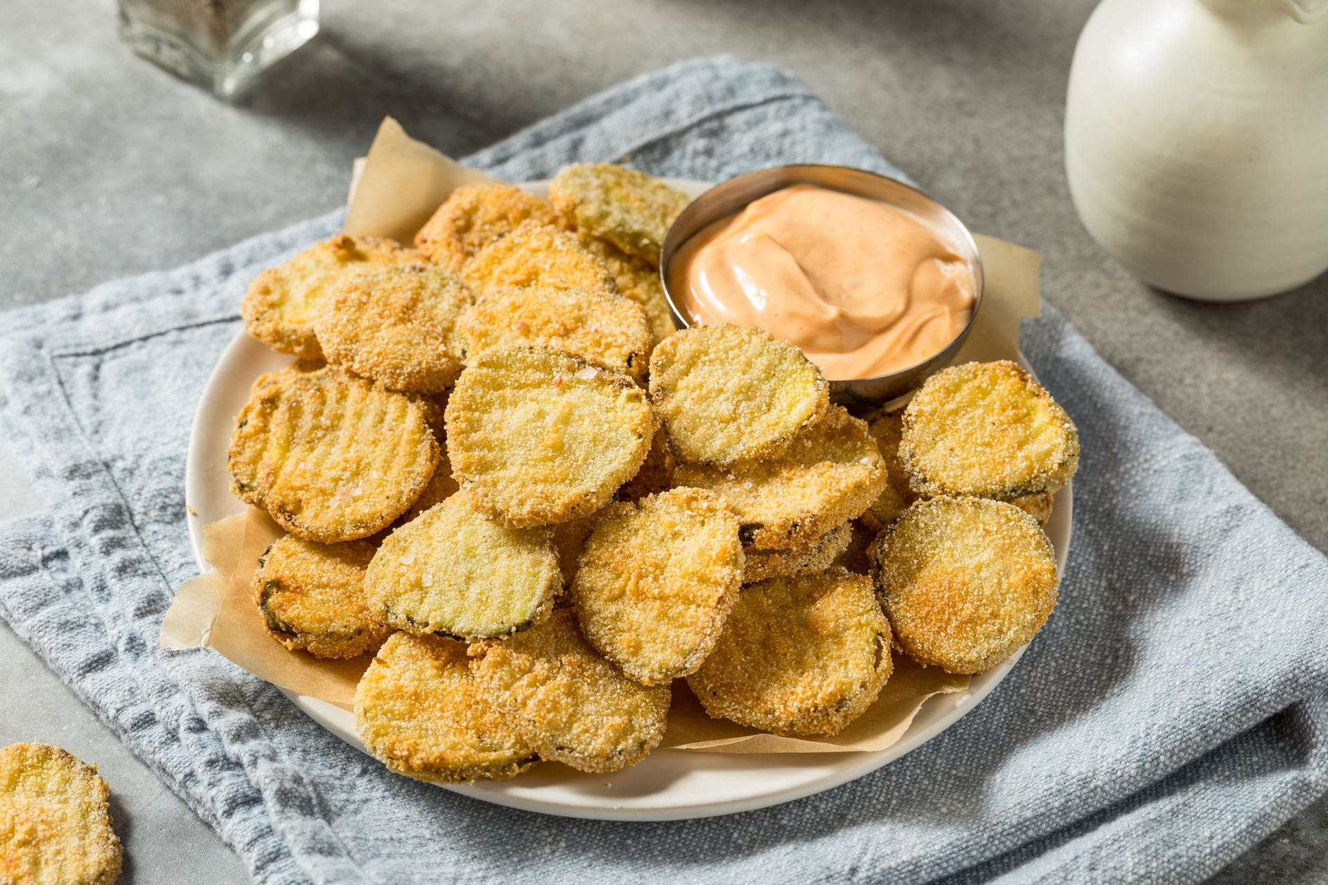 Breaded chicken nuggets on a plate with dipping sauce, served on a gray cloth napkin.