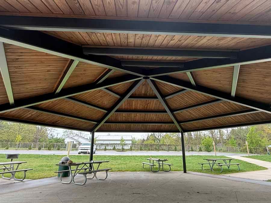 Covered pavilion with picnic tables in a park overlooking a grassy field and path