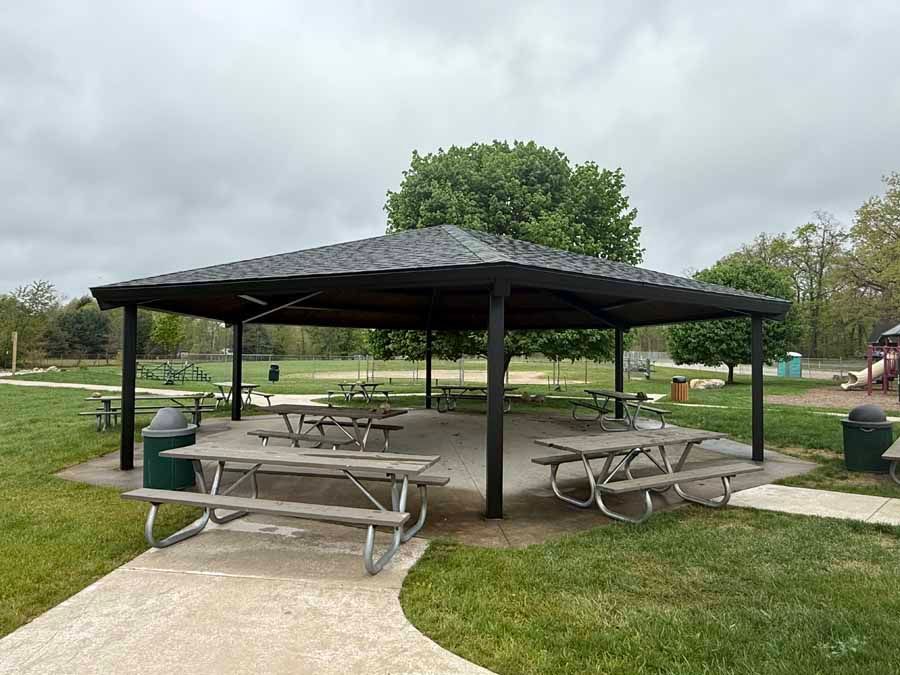 Park pavilion with picnic tables in a grassy park on a cloudy day