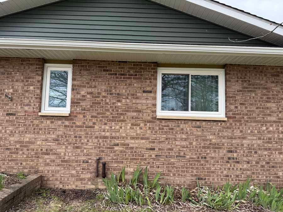 Brick house exterior with two windows and a small garden bed below the wall