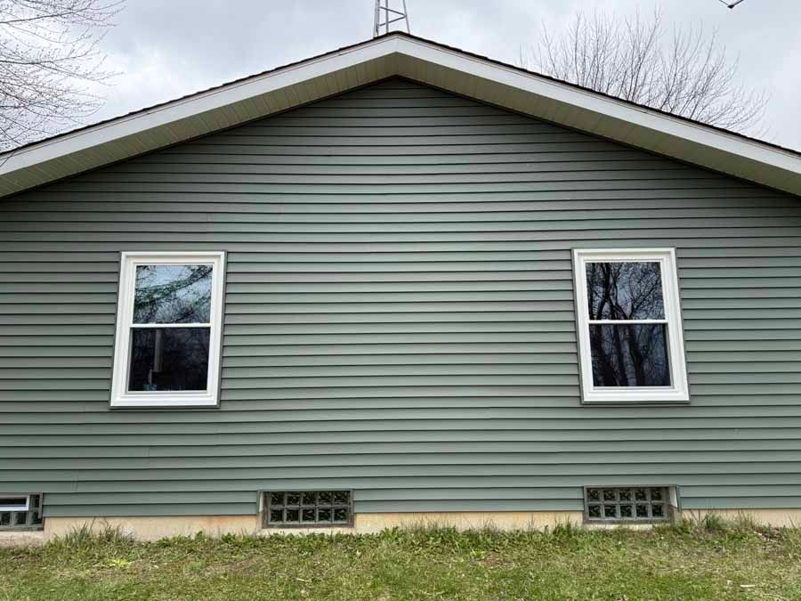 Gray house side wall with two white-framed windows and a gabled roof.